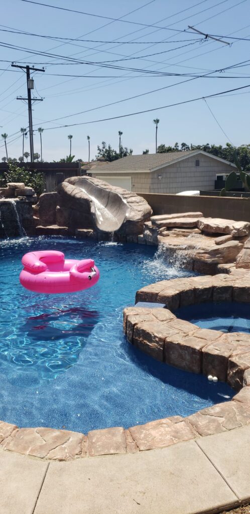 Blue swimming pool with artificial rock coping, rock slide, waterfalls and a rock-edged spa