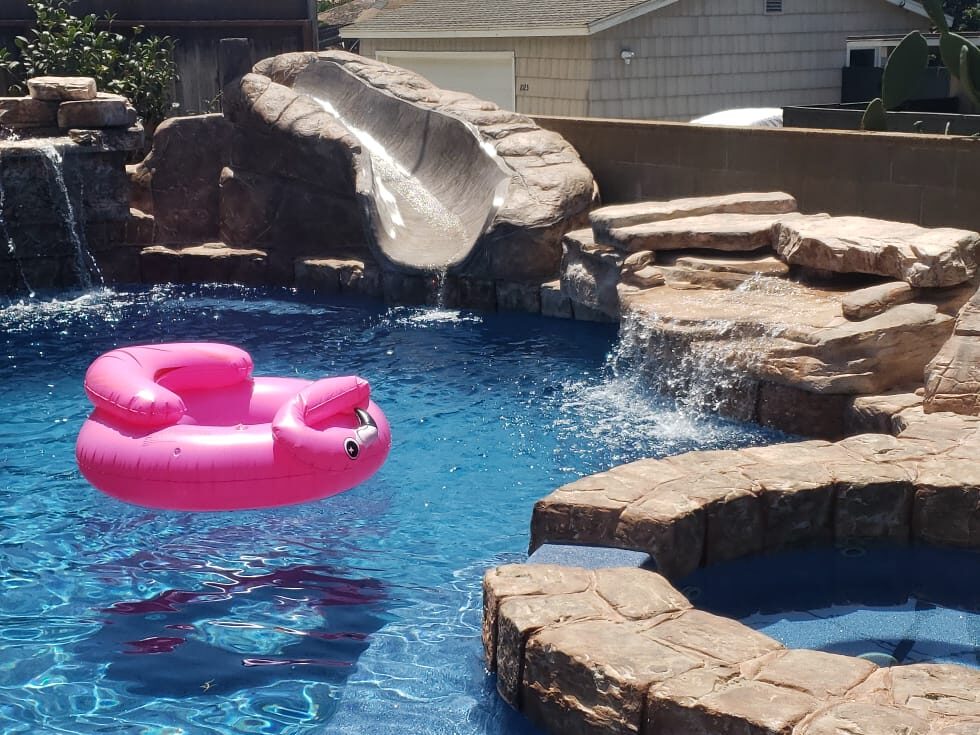 Blue swimming pool with artificial rock coping, rock slide, waterfalls and a rock-edged spa