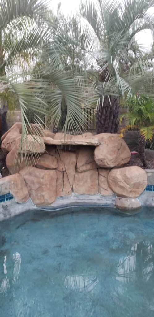 Artificial rock grotto water feature beneath palm trees at the edge of a spa