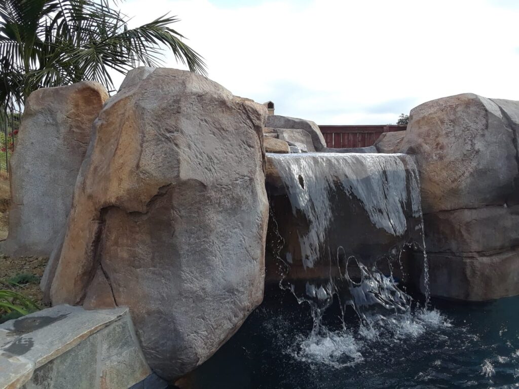 Sheet waterfall spilling between large sculpted artificial boulders into a swimming pool
