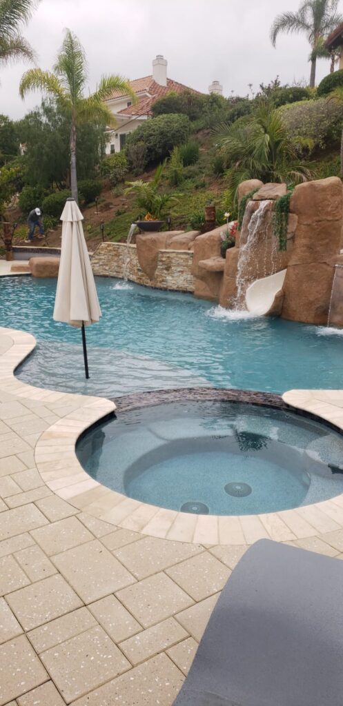 Finished backyard pool with artificial rock waterfalls, a rock slide, spa and a landscaped hillside