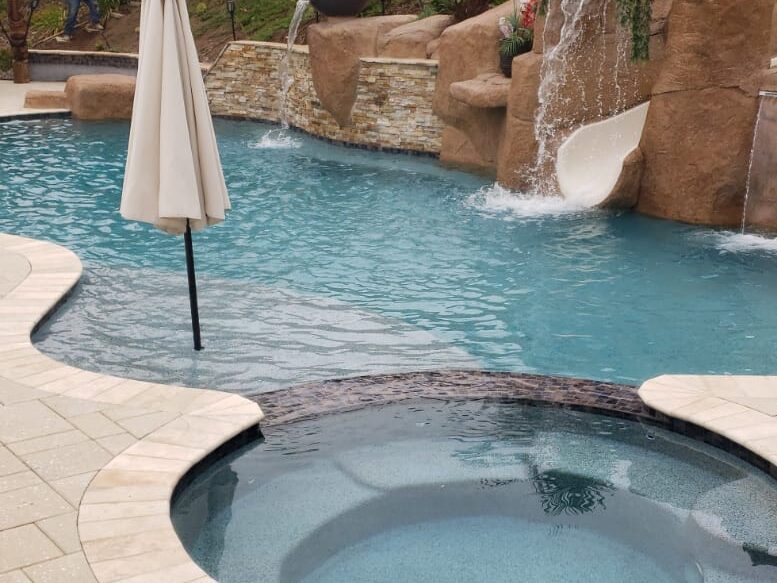 Finished backyard pool with artificial rock waterfalls, a rock slide, spa and a landscaped hillside