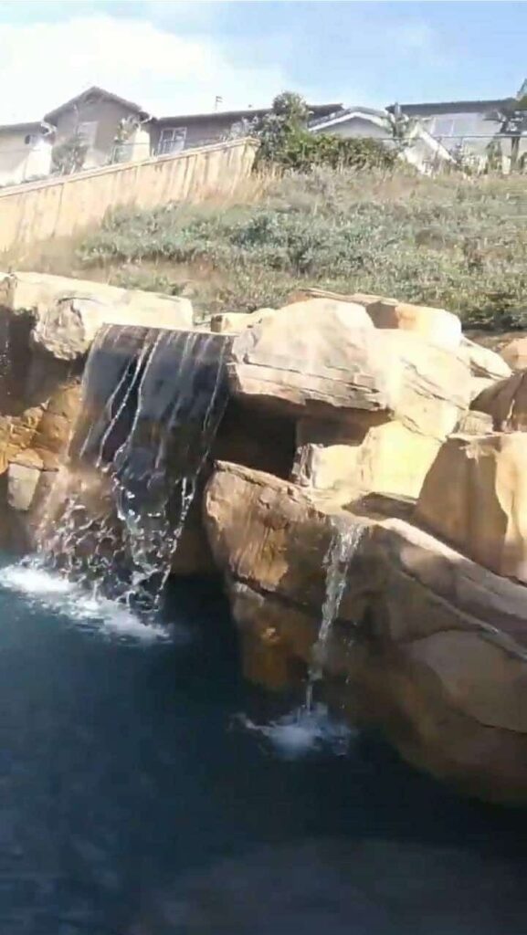 Tan sandstone-style artificial rock ledges with two waterfalls spilling into a pool